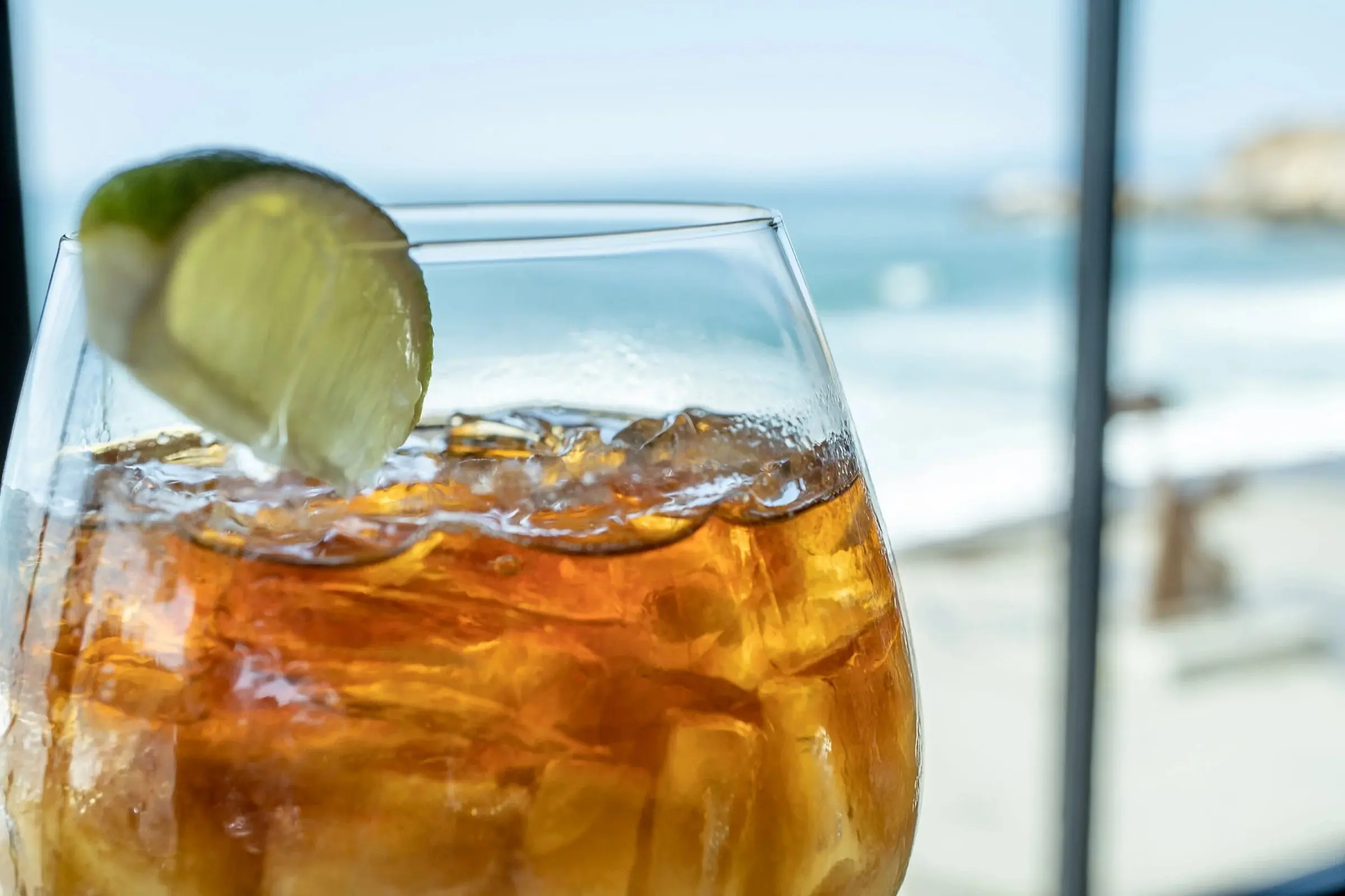 An iced cocktail with a lime wedge against a bright ocean view