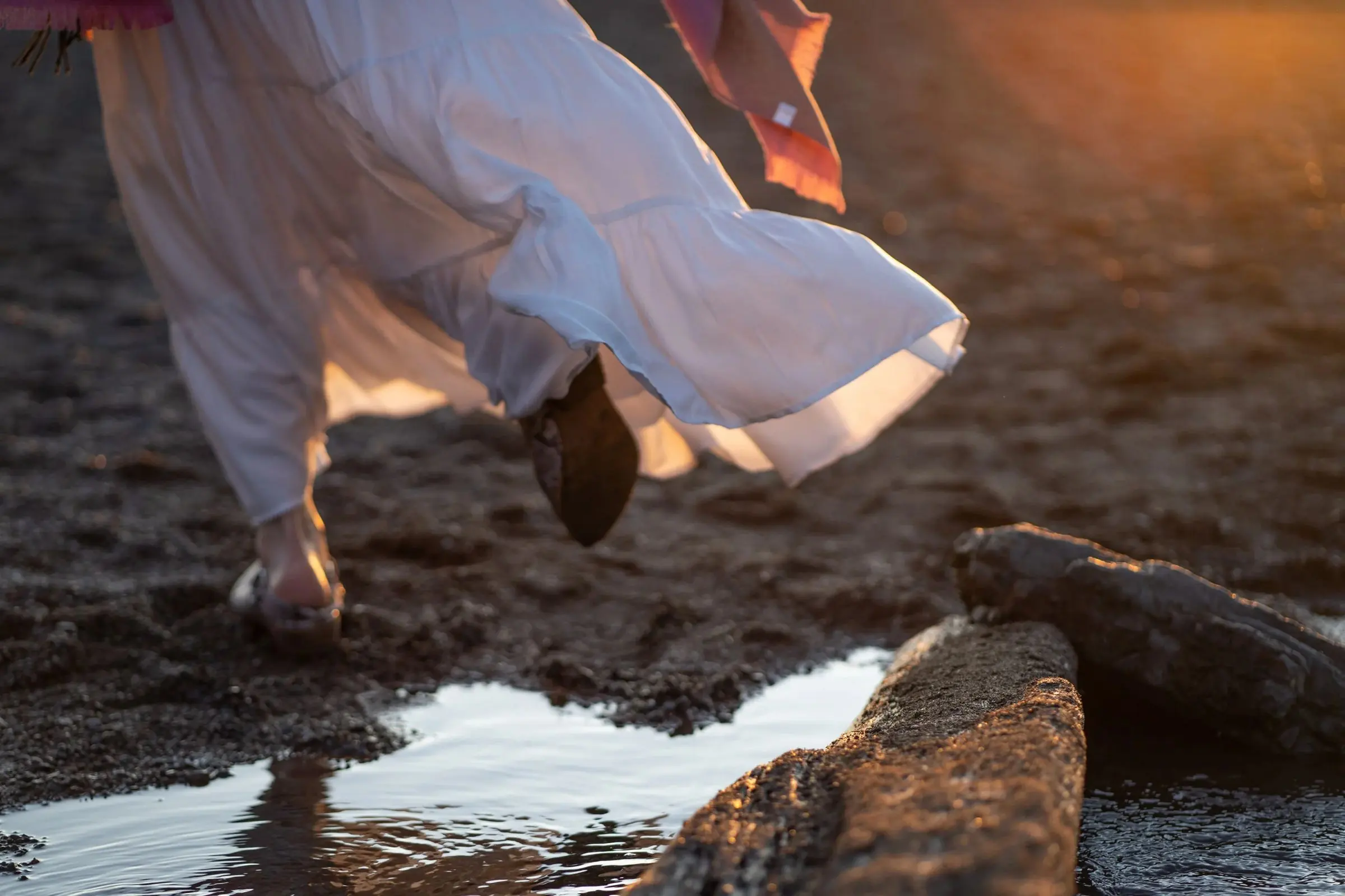A white dress sweeping past sunlit rocks and a tide pool