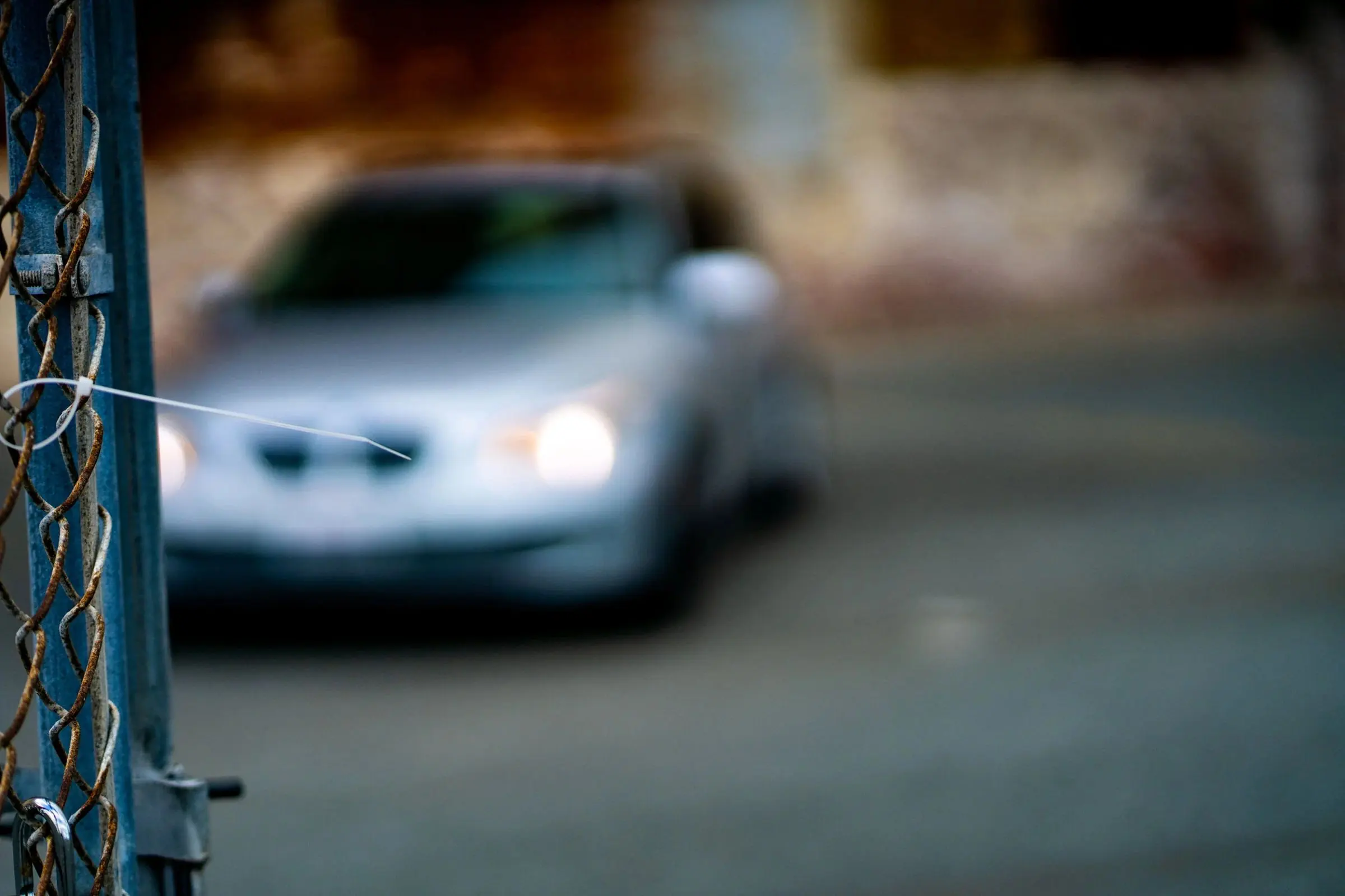 A silver sedan seen soft-focus through a chain-link fence